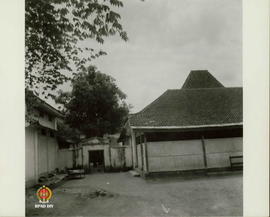 Lorong gapura yang diapit dua bangunan sebelah kanan pendapa yang tertutup dan sebelah kiri bangu...